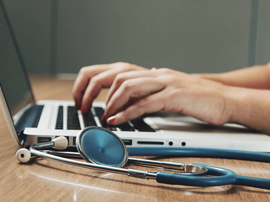 Person works on a laptop and next to it is a stethoscope