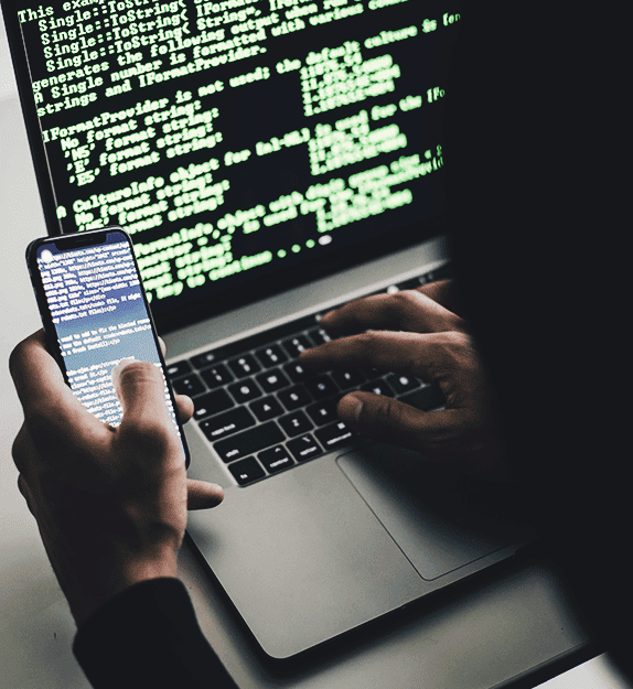 Person on laptop and writing code with a cell phone in hand