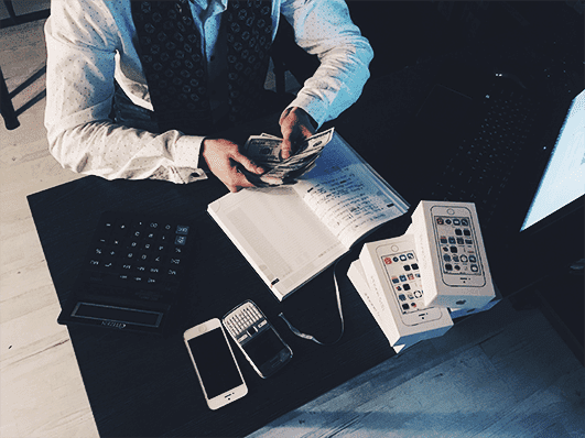 Person holds money in hand and sits in front of notebook and several cell phones