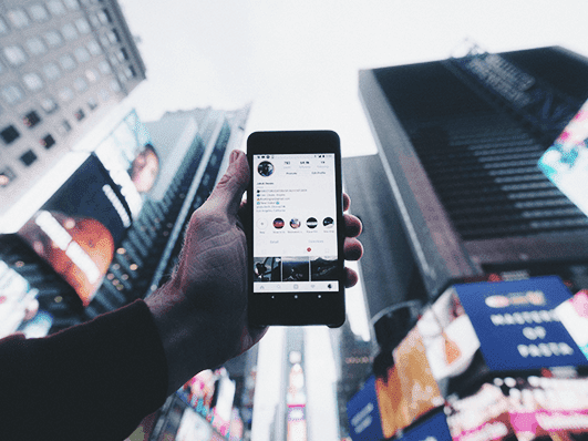 Hand holding up a cell phone and skyscrapers in the background