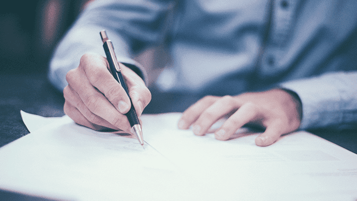 Pen in one hand and writes on paper