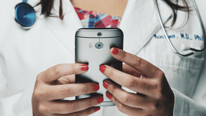 Frau im Arztkittel mit Stethoskop und Handy in der Hand